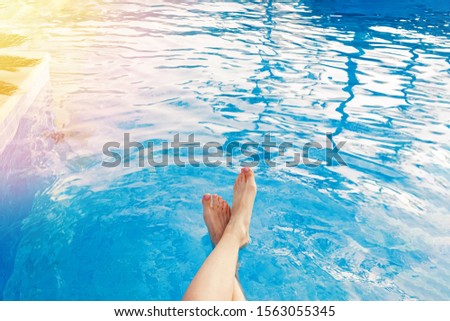 Woman's feet touching the water in swimming pool close-up