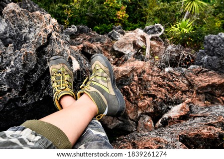 A woman's foot in hiking boots is sitting on a rocky mountain.