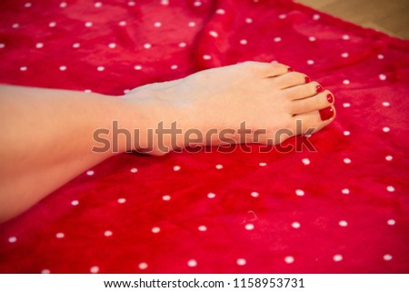 woman's foot on red carpet with nails with red nail polish. The carpet is reminiscent of Christmas.