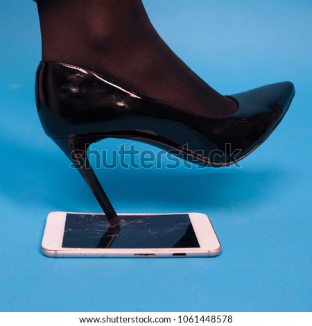 Woman's foot wear in high heel shoes smashes the mobile phone. Interesting advertisement photo for repair service.