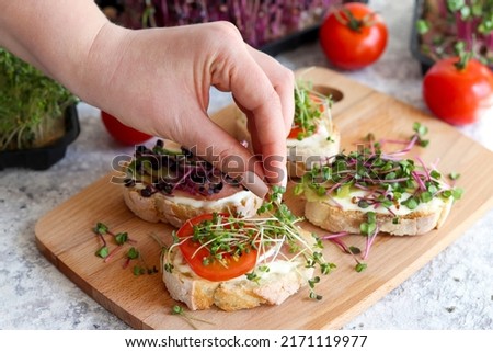 Woman's hand adding microgreens to toasts or bruschetta. Healthy, vegan food and dieting concept. Selective focus, close-up