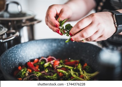 Woman's hand adds green herbs on grilled vegetables in a cast iron grilling pan. Stir fried vegetables in the pan. Fresh sliced vegetables close up.