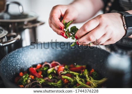 Woman's hand adds green herbs on grilled vegetables in a cast iron grilling pan. Stir fried vegetables in the pan. Fresh sliced vegetables close up.