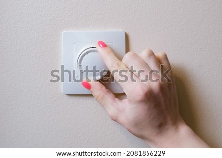 Woman's hand adjusts the lighting with a dimmer lever. An electronic device designed to change electrical power. Used to adjust the brightness of the light emitted by incandescent lamps or LEDs.