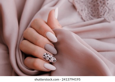 Woman's hand with a beautiful oval-shaped manicure. Autumn trend, beige color polishing with leopard pattern on nails with gel polish, shellac.