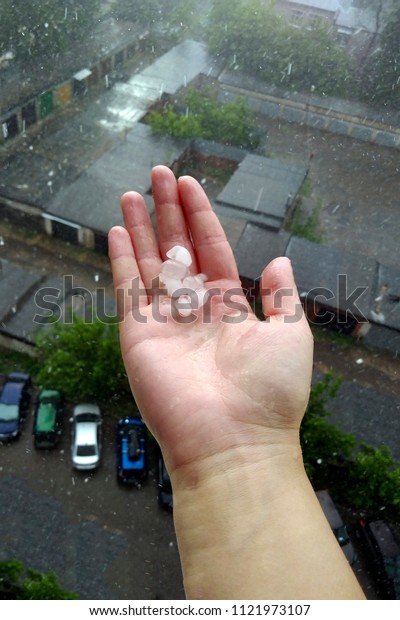 Woman\'s hand with big hail pieces catching rain\
drops through the balcony\
window