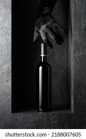 A Woman's Hand In A Black Glove Reaches For A Bottle Of Red Wine. A Concept Image On The Theme Of Expensive Wines.