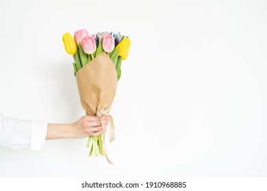 Woman's hand with a bouquet of colorful tulips against white wall - Shutterstock ID 1910968885