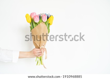 Woman's hand with a bouquet of colorful tulips against white wall