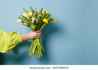 woman's hand with a bouquet of tulip flowers on a clean blue background - Powered by Shutterstock