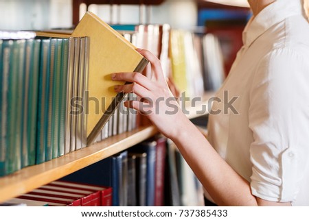 A woman's hand chooses a book in the library.