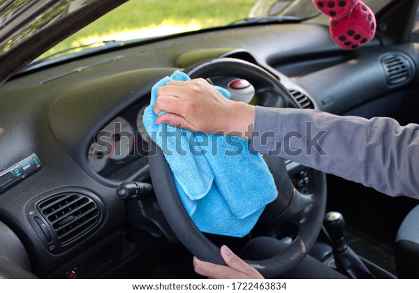 woman\'s hand cleaning steering wheel against virus\
with microfibre wipe