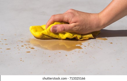 woman's hand cleaning tea stain or spilled coffee on a cement floor with a yellow floor cloth dishcloth closeup