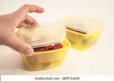 A Woman's Hand Closes The Lunchbox, The Photo Shows A Hand And Two Yellow Lunchboxes With Raspberries, Selective Focus