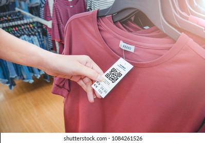 Woman's Hand With A Cloth Hang Tag Label With QR Code In A Clothing Shop Lighting Effect.