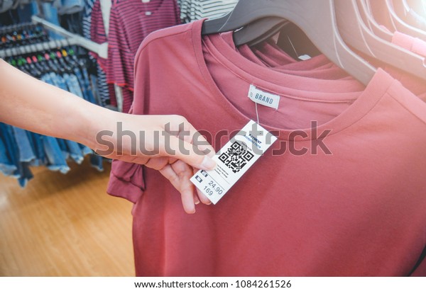 Woman\'s hand with a cloth hang tag label\
with QR code in a clothing shop lighting\
effect.