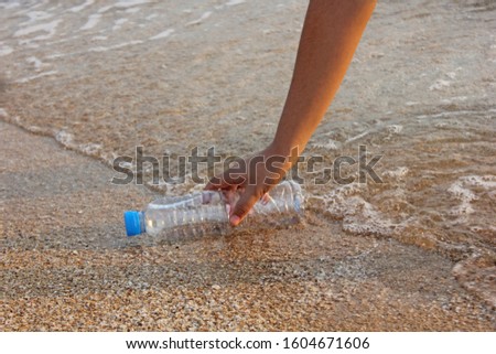 woman's hand collects plastic bottle on beach background. cleaning up beach. picking up plastic water bottle from the sandy beach. 