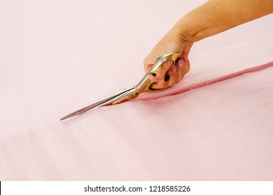 Woman's Hand Cuts Pink Fabric With Scissors.