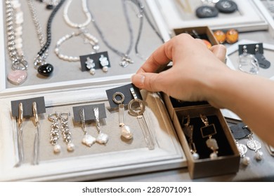 woman's hand delicately selects a handmade earring from a display, showcasing an array of artisanal jewelry in the background. supporting local artisans, and unique fashion accessories - Powered by Shutterstock