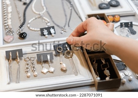 woman's hand delicately selects a handmade earring from a display, showcasing an array of artisanal jewelry in the background. supporting local artisans, and unique fashion accessories