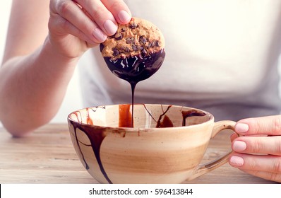 Womans hand dipping cookie in  melted dark  chocolate.
