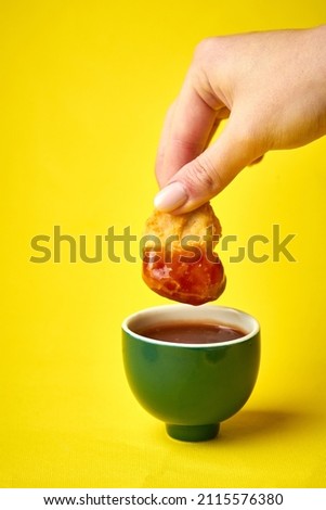 Woman's hand dips chicken nuggets in red sauce on yellow background