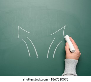 woman's hand drawn two arrows that diverge in different directions on a green chalk board, close up