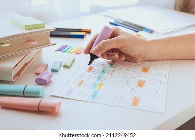 A woman's hand draws with a marker or purple text highlighter on a sheet with a schedule. Student workplace. Planning the week. Time management of pupil and student.