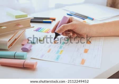 A woman's hand draws with a marker or purple text highlighter on a sheet with a schedule. Student workplace. Planning the week. Time management of pupil and student.