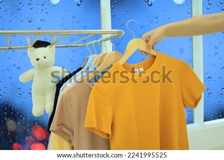 A woman's hand is drying clothes inside the house and water droplets on the glass of the window show that it is raining outside.