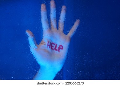 Woman's hand during the shower with the red word HELP. Symbolism against violence, abuse. Blue foggy blackground with water droplets on the glass. 