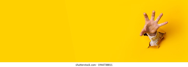 Woman's hand is extended and grabs something from a hole in the wall against a yellow background. Banner.