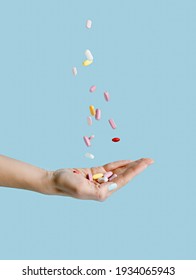 Woman's hand with falling medical pills isolated on pastel blue background. Creative close up pharmacy or health care concept. Medical treatment for disease flu virus.