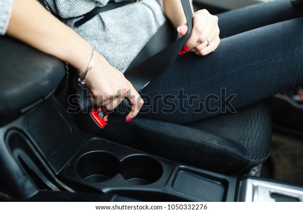 The woman\'s hand is fastened with a seat belt\
to start driving on the Car. Closeup image of a woman sitting in\
car and putting on her seat\
belt