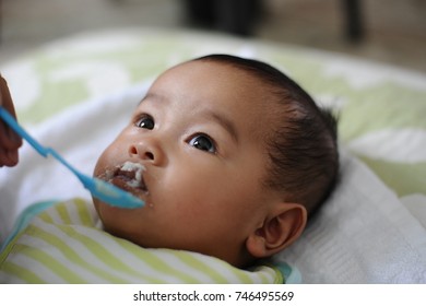 Woman's Hand Feeding Food To Little Baby Girl.New Born Baby Girl Wearing Napkin While Eating Cereal.