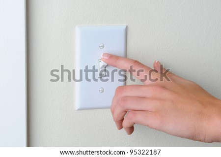 Womans hand with finger on light switch, about to turn off the lights. Closeup of hand and switch only. Horizontal format.
