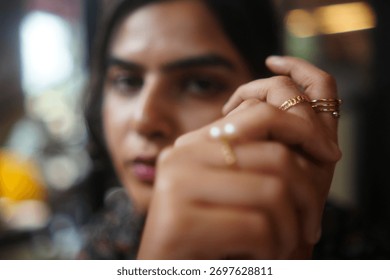 A woman's hand is in focus, displaying multiple gold rings, with a blurred face in the background