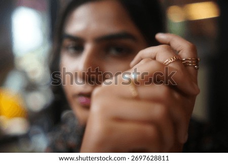 A woman's hand is in focus, displaying multiple gold rings, with a blurred face in the background