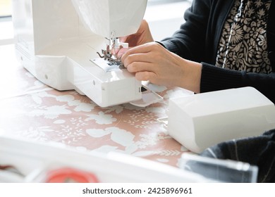 Woman's hand in front of the sewing machine to thread the needle and then sew. Precision and minute detail.