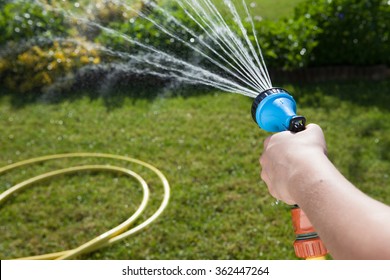 Woman's hand with garden hose watering plants, gardening concept