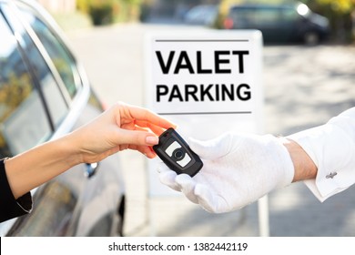 Woman's Hand Giving Car Key To Male Valet Near Valet Parking Sign