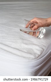 Woman's Hand With A Glass Of Water Above The Mattress In A Waterproof Case