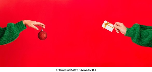 woman's hand in a green sweater holds the symbol of the New Year - a red Christmas ball. Web banner - Powered by Shutterstock