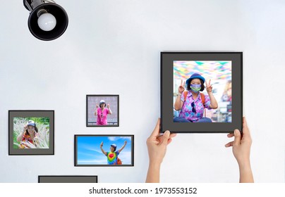 Woman's Hand Hanging Her Portrait Photo In Protective Mask While Outdoors Traveling During Coronavirus Outbreak Time On The Wall In Her Room With Many Photo Frames In Normal Life Time	