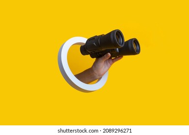 Mano de mujer sosteniendo binoculares en un agujero de fondo amarillo 