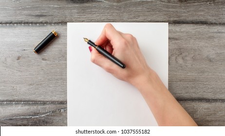 Woman's hand holding black fountain pen ready to write on blank paper on gray wooden desk