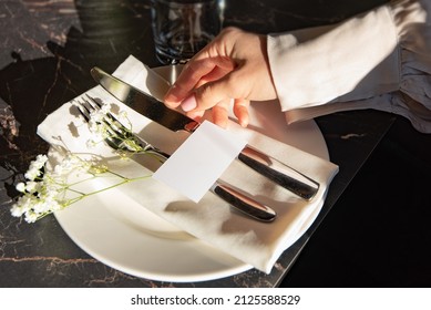 Woman's hand holding blank business card against plate with fork and knife on black - Shutterstock ID 2125588529