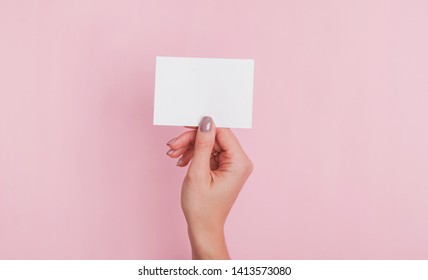 Woman's Hand Holding Blank Paper Card Against The Pink Wall