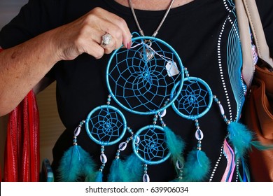 Woman's Hand Holding Blue Dream Weaver Feather Design Against Her Black Shirt