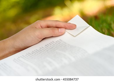 Woman's Hand Holding A Book While Folding Down The Corner Of A Page / Dog-earing A Book Page.